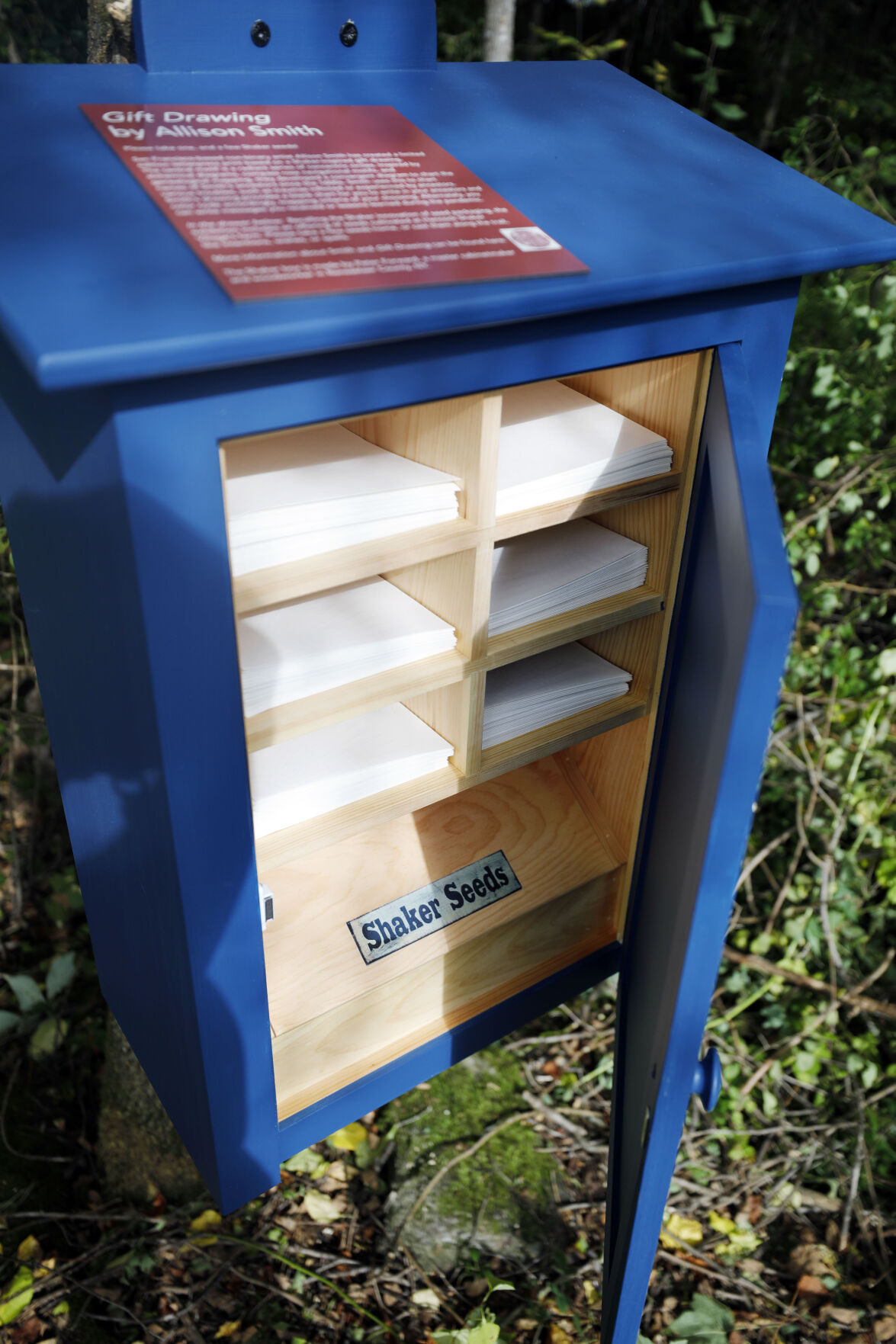 blue box with papers and seeds inside attached to tree